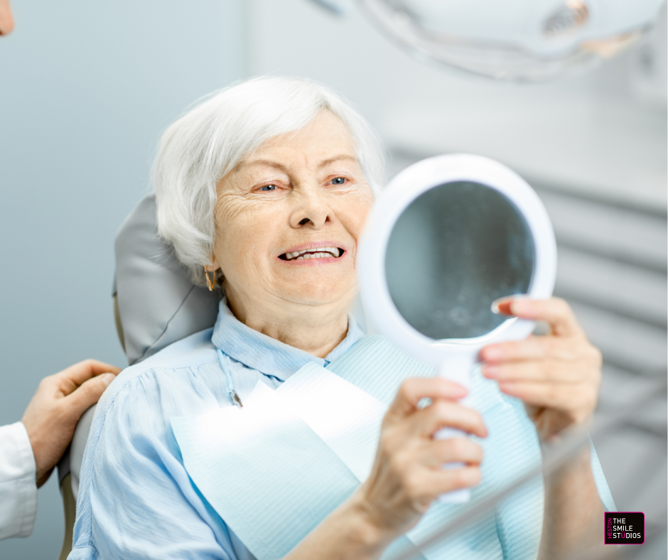 Elderly lady checking her new dentures in the mirror at the dentist.
